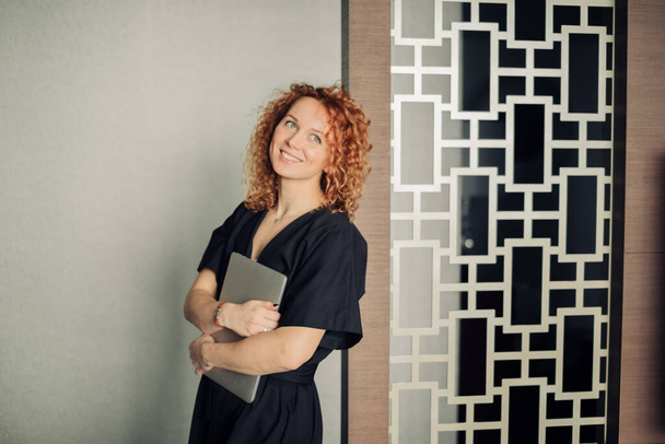 Woman in stylish black overalls with curly ginger hair posing with laptop - Zdjęcie, obraz
