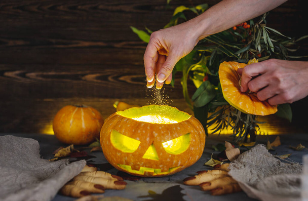 Hand is pouring glowing powder into a pumpkin with a carved face to make a potion. Concept of celebrating Halloween and magic atmospheres. - Photo, Image