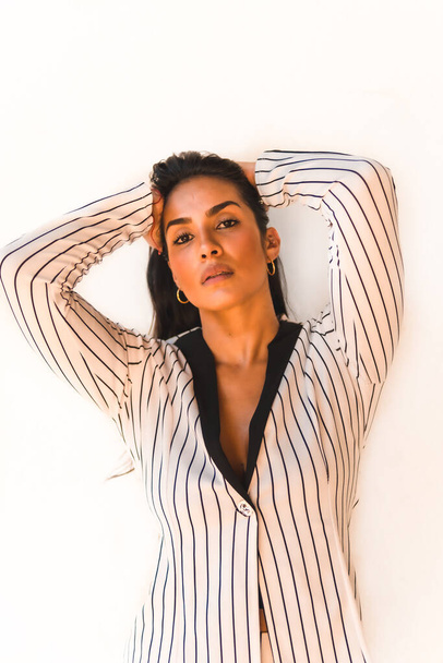 Lifestyle, straight-haired Latin brunette girl in a white suit and black stripes. On a white background. Looking at the camera, in different postures, fashion editorial - Photo, Image