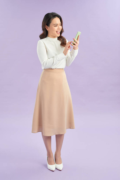 Retrato de una chica alegre mirando el teléfono móvil aislado sobre fondo púrpura - Foto, imagen