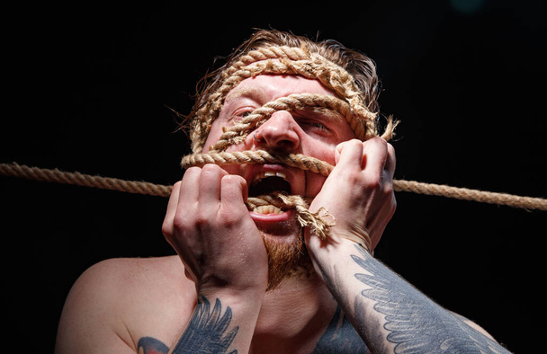 Photo of binded tattooed man trying tear the rope on face - 写真・画像