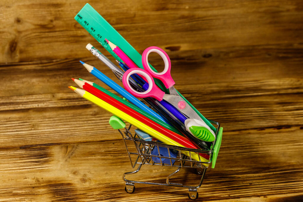 Buying school supplies. Shopping cart with school supplies on a wooden background. Back to school concept - Фото, изображение