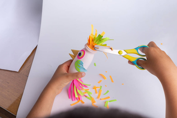 niño hace una artesanía de papel y botella de yogur reciclado, papagayo de papel DIY. Jardín de infantes y actividades escolares - Foto, imagen