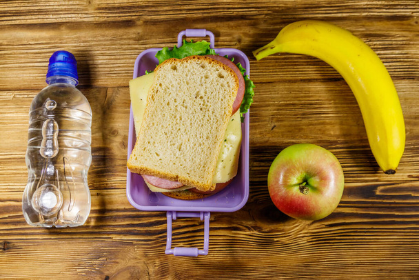 Pranzo con panini, bottiglia d'acqua, banana e mela su un tavolo di legno. Vista dall'alto - Foto, immagini