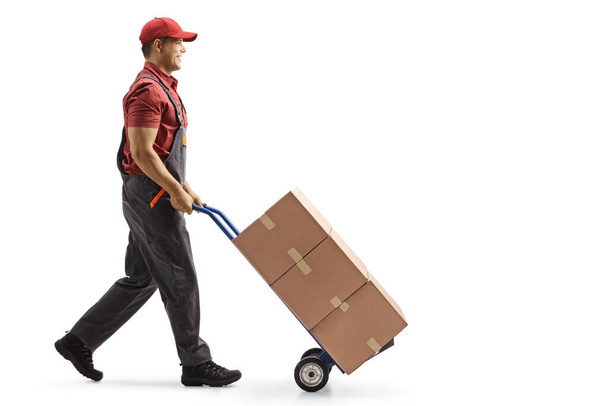 Full length profile shot of a male worker pushing boxes on a hand-truck isolated on white background - Fotografie, Obrázek