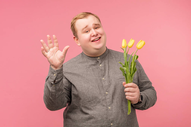 Homme drôle avec des fleurs va faire une proposition, a regard joyeux et sourire naïf - Photo, image