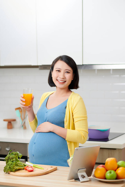 Donna incinta con bicchiere di succo d'arancia in cucina - Foto, immagini