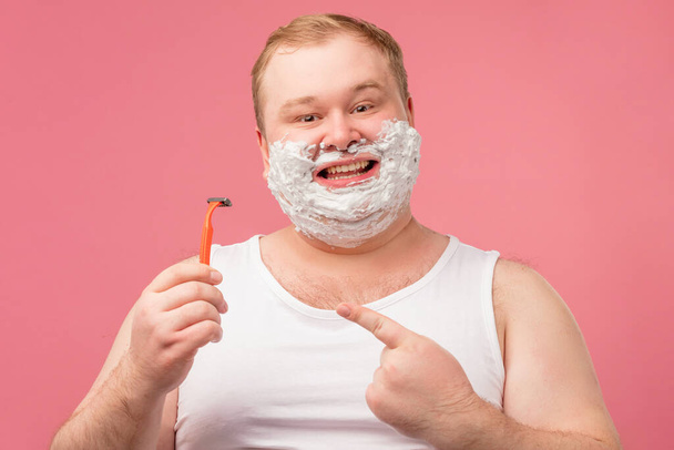 Happy plump man with shaving foam on his face and razor isolated on pink - Fotografie, Obrázek