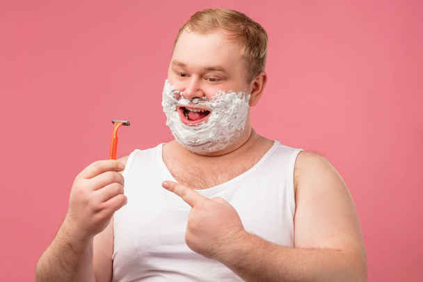 Happy plump man with shaving foam on his face and razor isolated on pink - Фото, изображение