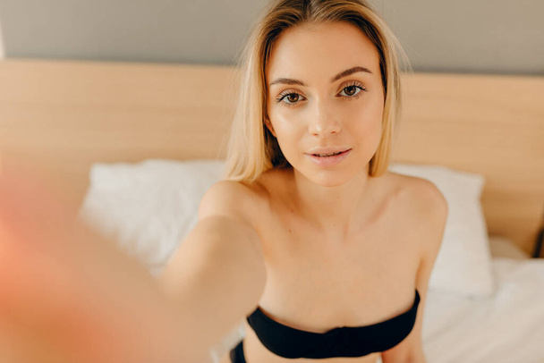 Sensual blonde woman in black underwear looking at camera while lying in bed - Foto, Bild