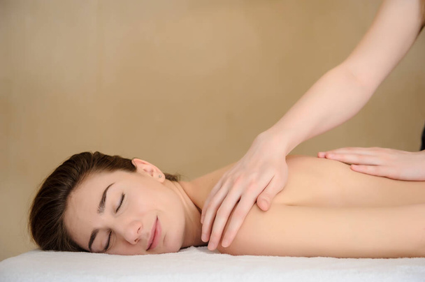 vista lateral de una joven recibiendo un masaje de cuello y hombros realizado por una masajista en un salón de spa - Foto, Imagen