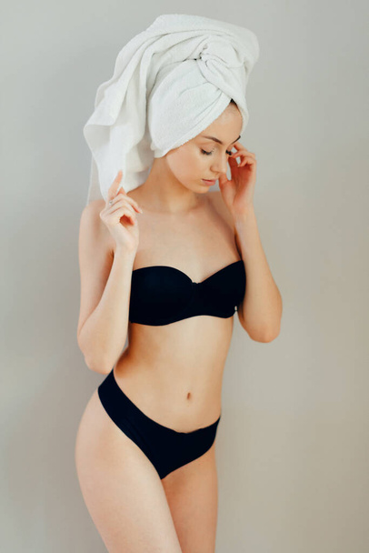 Woman in black lingerie posing with towel on head over light background - Фото, изображение
