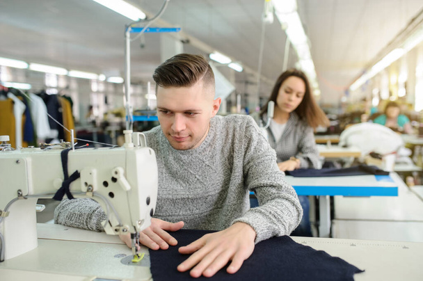 cerca de la foto de un joven y otras costureras cosiendo con la máquina de coser en una fábrica - Foto, Imagen