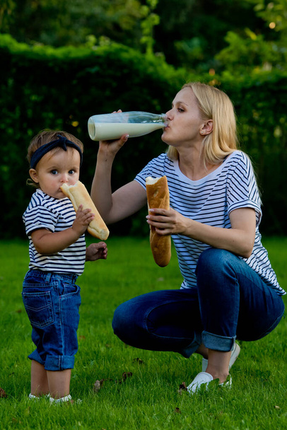 ジーンズの若い女性とストライプのTシャツは、ガラス瓶からミルクを飲みます。ファミリーピクニック. - 写真・画像