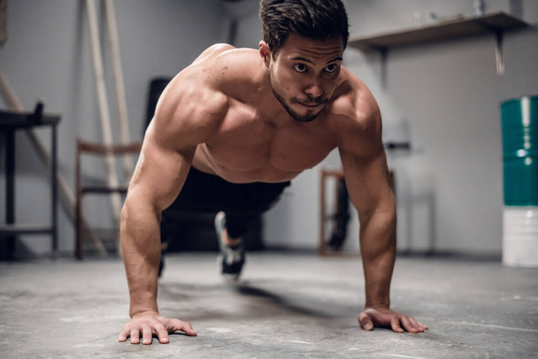 a muscular sportsman does push-UPS from the floor in the gym. - Photo, Image