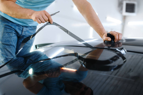 Мужская оболочка режет тонировку, тюнинг. Рабочий наносит виниловый оттенок на окно автомобиля в гараже, тонированное автомобильное стекло - Фото, изображение