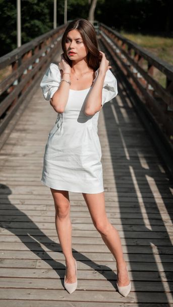 Beautiful young sexy girl with long brunette hair with a bright evening make-up perfect summer tan thin figure dressed in white silk dress with lace and high heels shoes businesswoman casual clothes - Valokuva, kuva