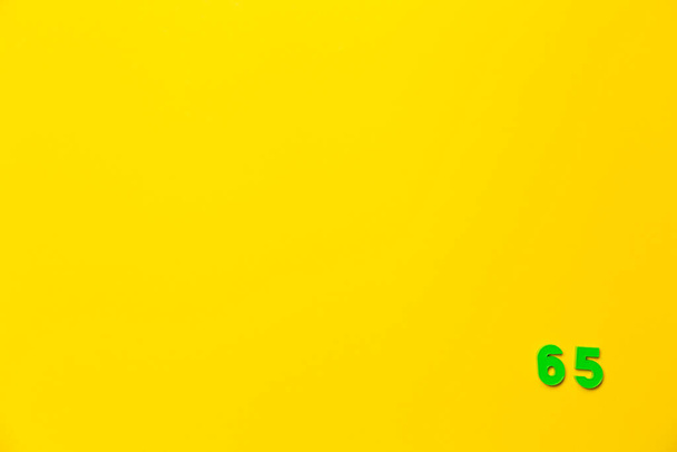 Zelená plastová hračka číslo šedesát pět je umístěna v pravém dolním rohu na žlutém pozadí. - Fotografie, Obrázek