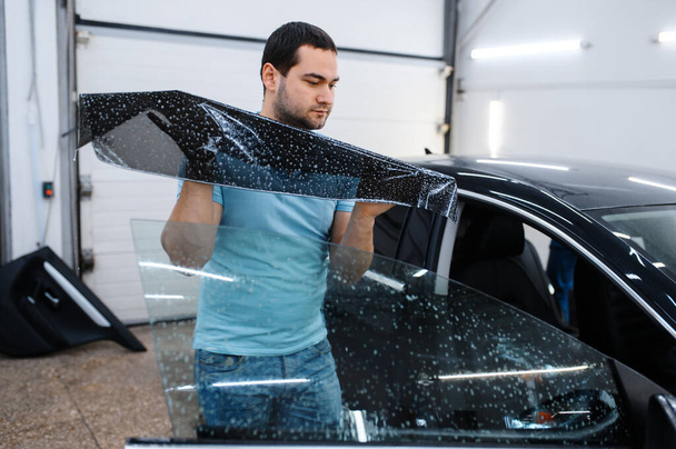 Male specialist installs wetted car tinting, tuning service. Mechanic applying vinyl tint on vehicle window in garage, tinted automobile glass - Photo, Image