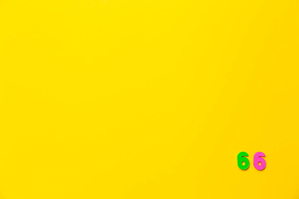 Un juguete de plástico verde y rosa número sesenta y seis se encuentra en la esquina inferior derecha sobre un fondo amarillo. - Foto, imagen