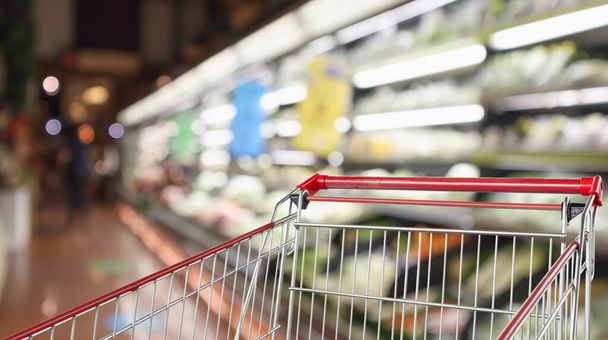 果物や野菜棚付きのスーパーマーケット食料品店の内部は空の赤いショッピングカートと背景に焦点を当てた - 写真・画像