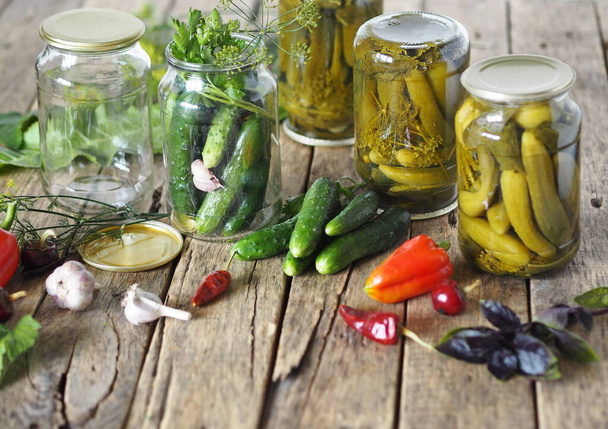 Jars with cucumbers, ingredients for pickling on a wooden ancient natural table. The process of preserving cucumbers in glass jars under lids for storage for the winter. - Φωτογραφία, εικόνα