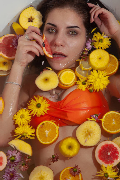 Attractive girl enjoys a bath with flowers and slices of citrus and fruits. soft focus - Photo, Image