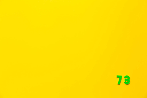 Зеленая пластиковая игрушка номер семьдесят три находится в правом нижнем углу на желтом фоне. - Фото, изображение