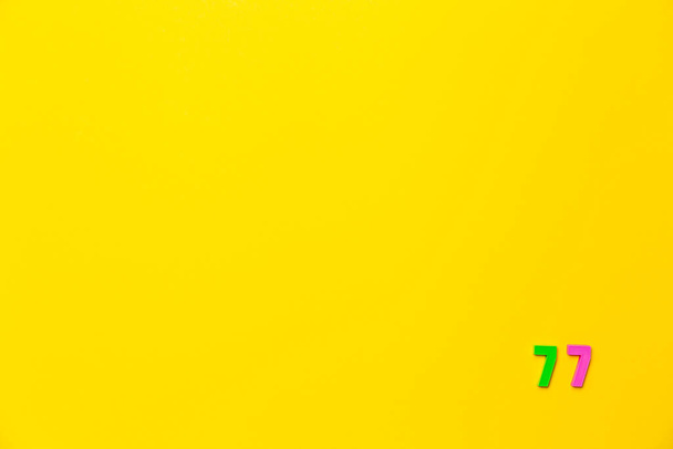 Um brinquedo de plástico verde e rosa número setenta e sete está localizado no canto inferior direito em um fundo amarelo. - Foto, Imagem