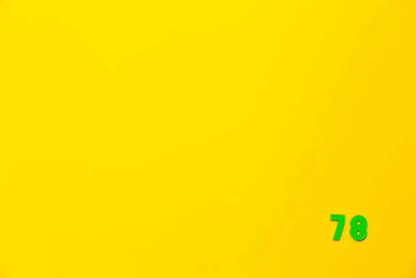 Un jouet en plastique vert numéro soixante-dix-huit est situé dans le coin inférieur droit sur un fond jaune. - Photo, image
