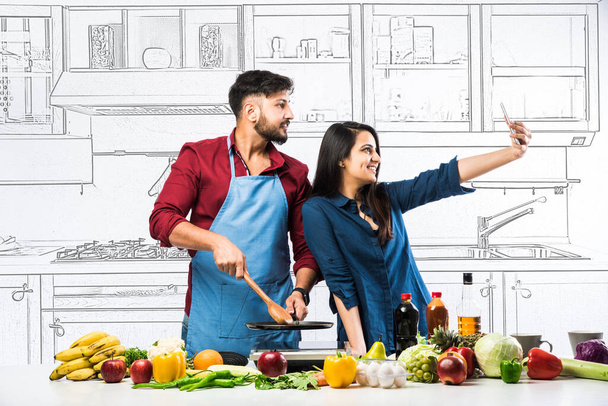 Indian couple in kitchen - Young Beautiful asian wife enjoying cooking with husband with lots of fresh vegetables and fruits - Photo, Image
