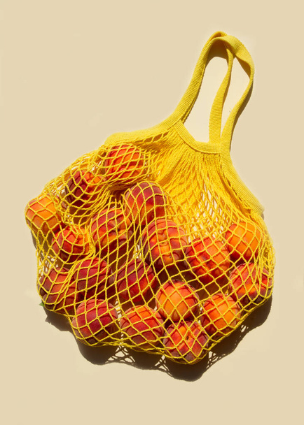 薄い黄色の背景にメッシュバッグやストリングバッグに桃を熟す。平置きだ。廃棄物ゼロ。トップ表示. - 写真・画像