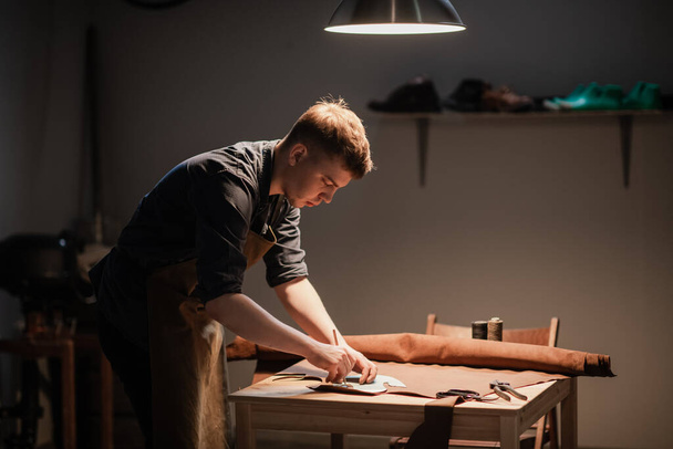 un joven aprendiz hace espacios en blanco para la producción de zapatos en el taller. - Foto, Imagen