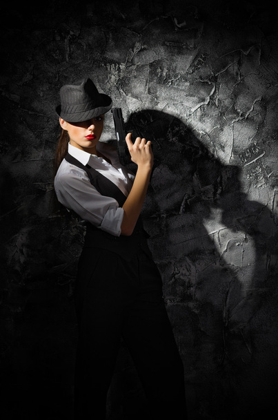 Portrait of young woman in manly style with gun at grey wall - Фото, изображение