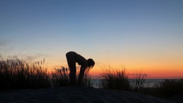 Nerozpoznatelná žena dělá jógu na pobřeží ve večerních hodinách - Záběry, video