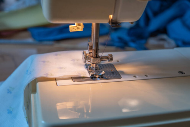 Un primer plano de la aguja de un material de costura de la máquina de coser juntos para hacer una máscara facial casera como la gente está obligada a usarlos debido a Covid 19 - Foto, imagen