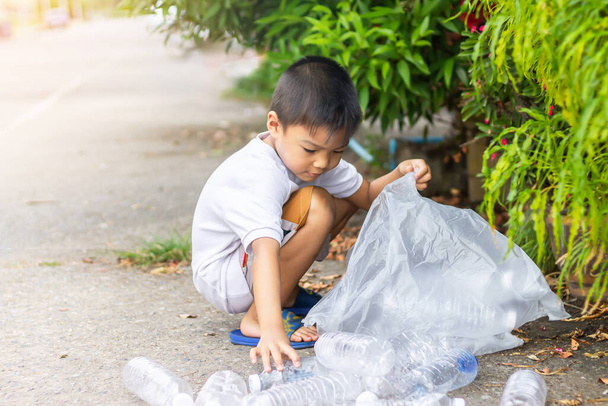 In het stadspark. Aziatische kind jongen is een vrijwilliger voor het opruimen van de veld vloer. Hij pakt veel plastic flesjes en stro op de grond. Bespaar het milieu en reduceer het afvalconcept. - Foto, afbeelding