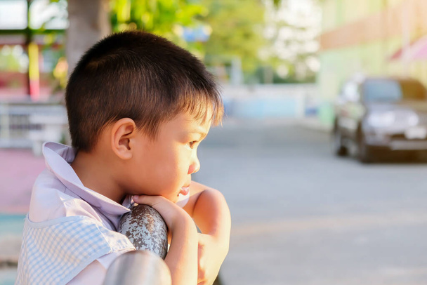 Retrato de un niño asiático sintiéndose triste. Él de pie en el patio de recreo y las manos sosteniendo una cerca de hierro. Expresión y emociones del concepto de niño. - Foto, imagen