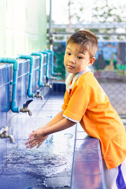 アジアの子供の男の子は食べ物を食べる前に手を洗って、学校の洗濯ボウルでおもちゃを果たした後。5歳の少年。ヘルスケアと子供の概念. - 写真・画像