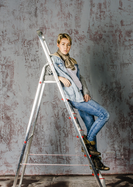 Young girl in jeans and jacket standing on the stairs stepladder and flirts - 写真・画像