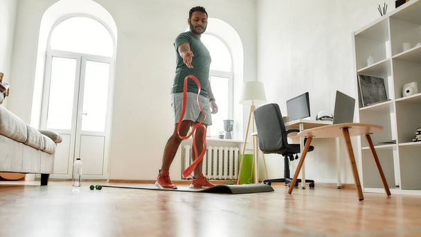 Finish training. Full length shot of young active man throwing resistance band after exercising with it during morning workout at home. Sport, healthy lifestyle - Φωτογραφία, εικόνα