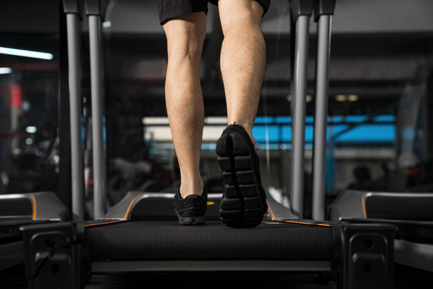 Крупним планом чоловічі ноги, що працюють на біговій доріжці в тренажерному залі, спортивні тренування, концепція життя людей
 - Фото, зображення