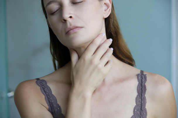 Genç bir kadın boğazına dokunuyor. Boğaz ağrısı, bademcik iltihabı ya da tiroit bezi sorunu.. - Fotoğraf, Görsel