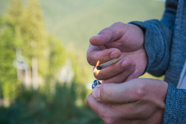 Close-up of young man smoking marijuana joint outdoors. Hemp blunt in the male hand. Cannabis is a concept of herbal and alternative medicine - Photo, Image