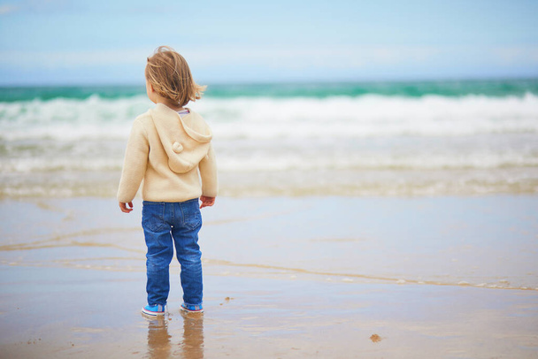 Adorable toddler girl on the sand beach at Atlantic coast of Brittany, France. Small child enjoying vacation by the sea or ocean. Travelling with kids - Photo, Image