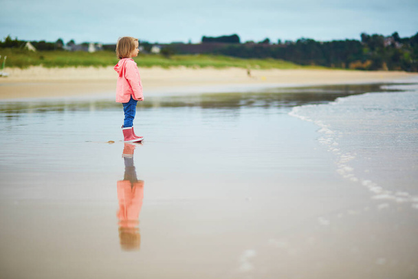 Adorable toddler girl on the sand beach at Atlantic coast of Brittany, France. Small child enjoying vacation by the sea or ocean. Travelling with kids - Φωτογραφία, εικόνα