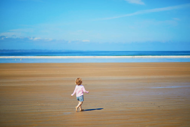 Adorable toddler girl on the sand beach at Atlantic coast of Brittany, France. Small child enjoying vacation by the sea or ocean. Travelling with kids - 写真・画像