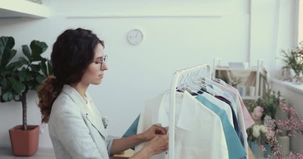 Young businesswoman organizing new female clothing collection on hangers. - Кадры, видео