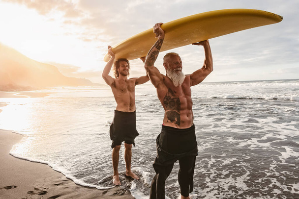 Amigos felices con diferentes edades surfeando juntos en el océano tropical - Gente deportiva divirtiéndose durante el día de surf de vacaciones - Personas mayores y jóvenes y el concepto de estilo de vida de deporte extremo - Foto, Imagen