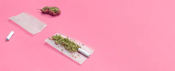 Marijuana and materials to roll a cannabis joint isolated on pink background with copy space right. - Photo, Image